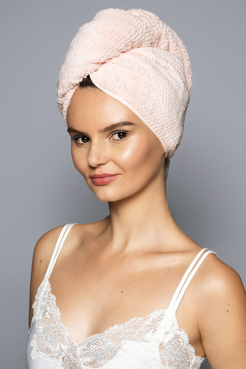 Woman wearing a pink towel on her head against a gray background