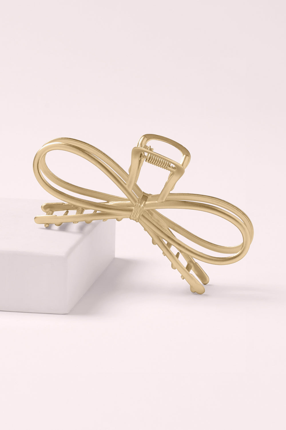 Gold bow-shaped hair clip on a pink background1