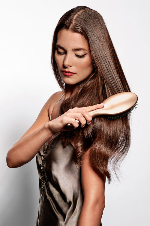 brunette model with gold brush brushing her hair