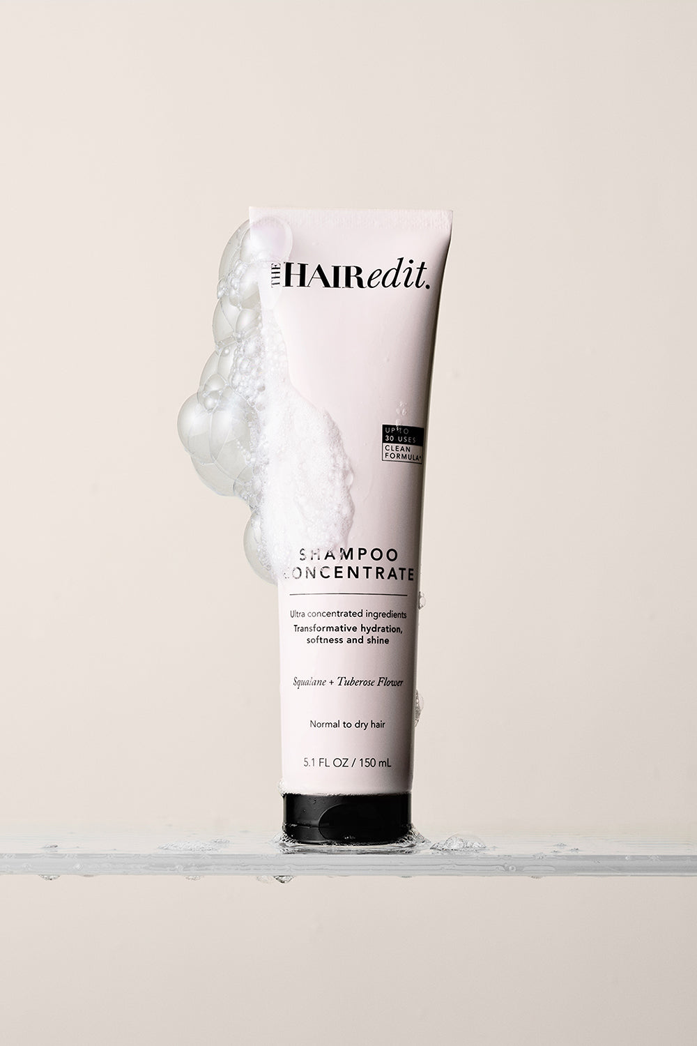 The Hair Edit Shampoo Concentrate Tube on a Beige Background with foam bubbles on the side of tube12