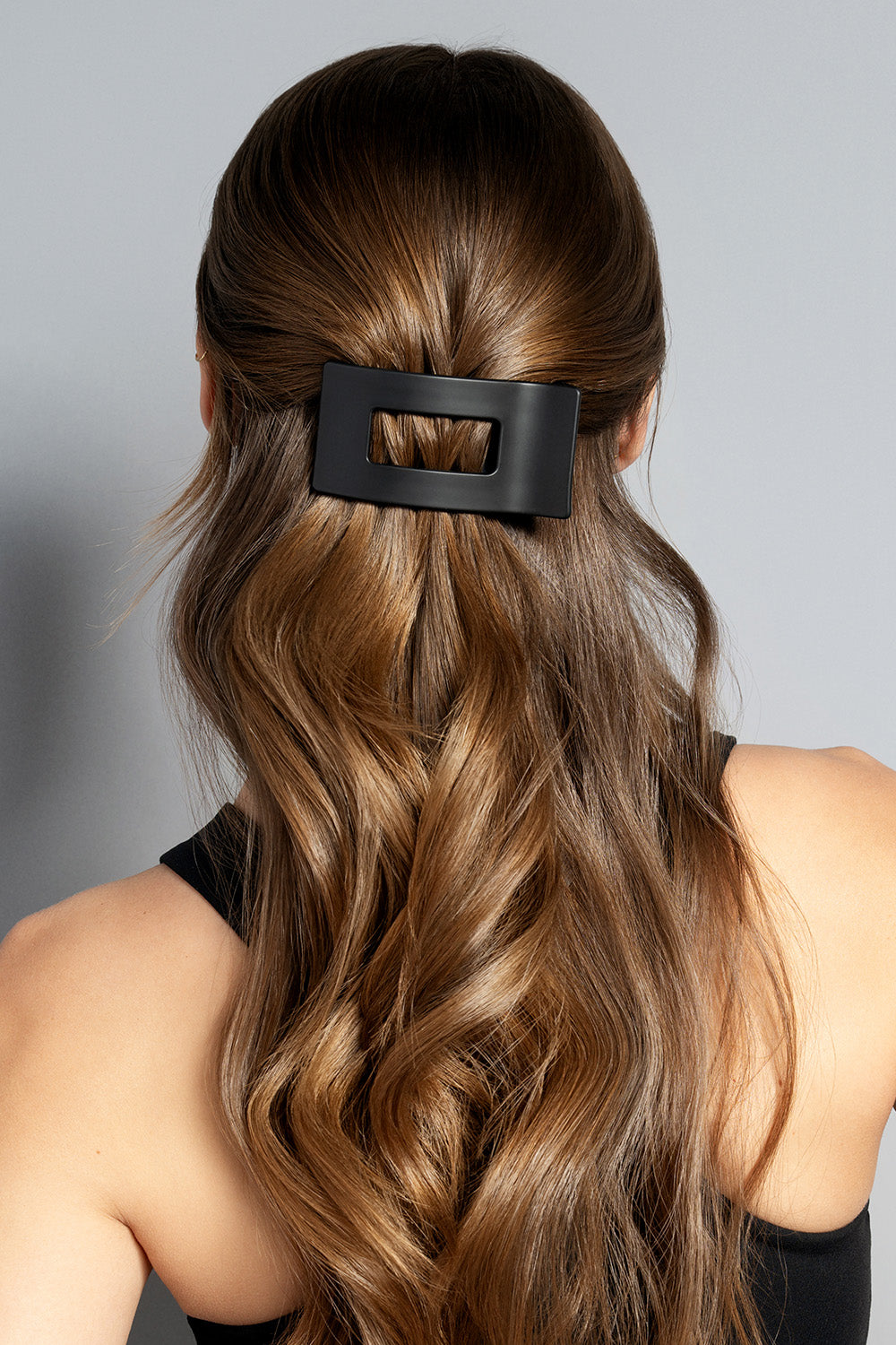 A brunette model with long wavy hair wearing a black rectangle flat lay claw clip on a gray background3