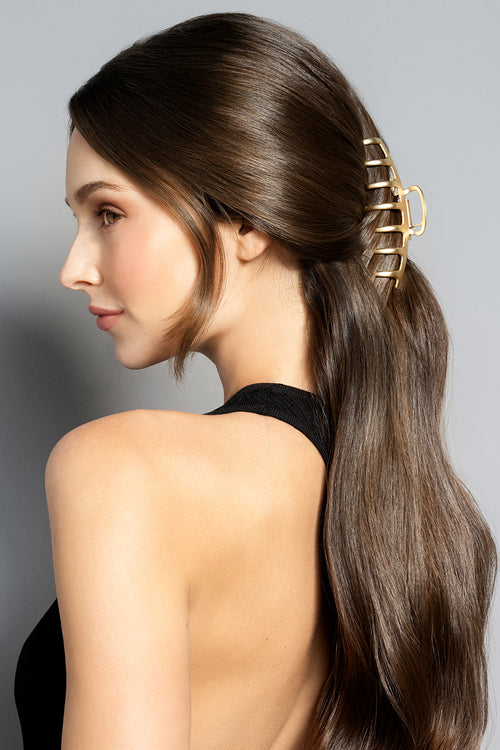 Woman with long brown hair styled with a gold hair clip against a gray background