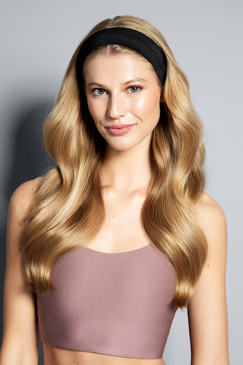 Woman with long blonde hair wearing a black headband against a gray background