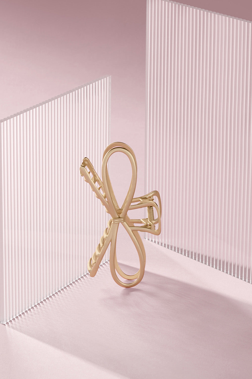 Gold bow-shaped hair clip on a light pink background4
