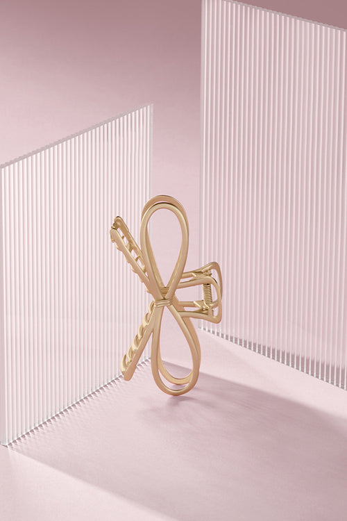 Gold bow-shaped hair clip on a light pink background