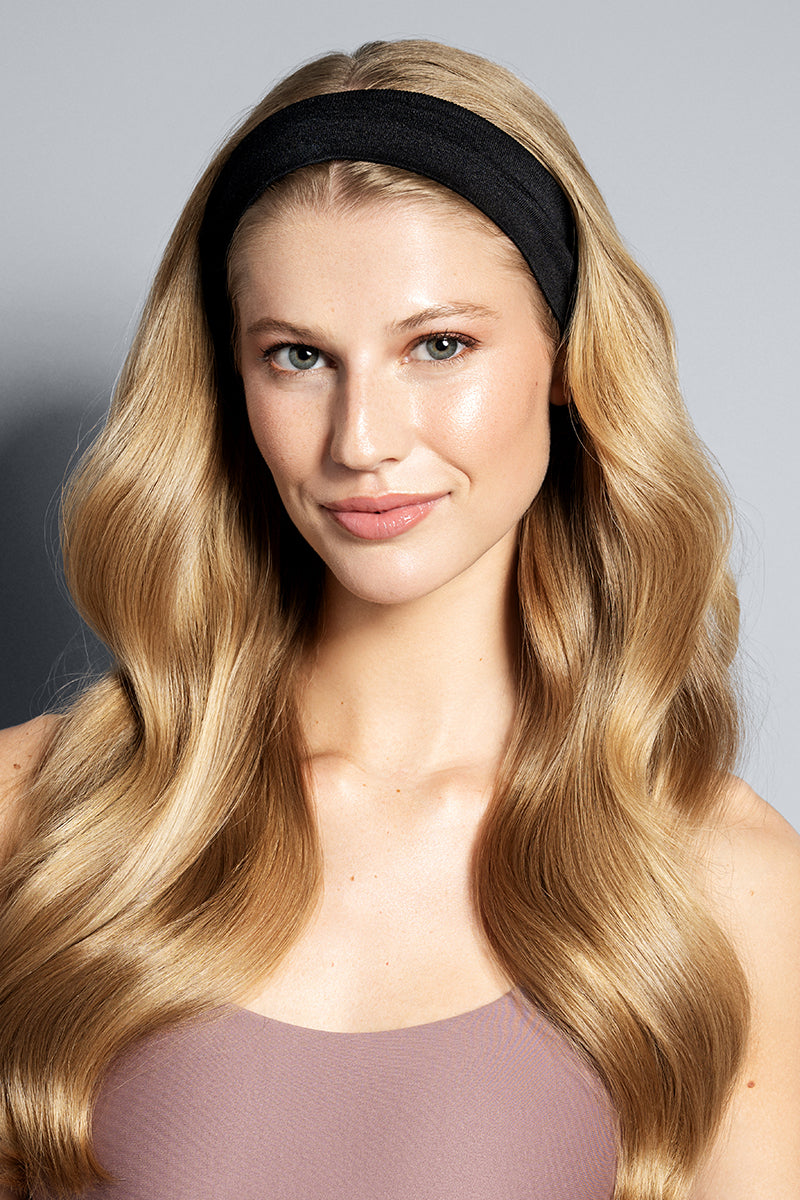 Woman with long blonde hair wearing a black headband against a gray background
