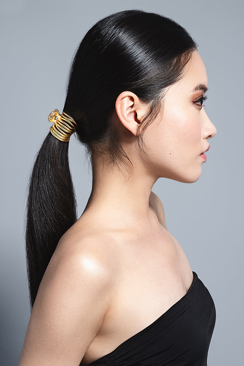Woman with a dark hair ponytail wearing a gold hair Gilded Wrap Clip 