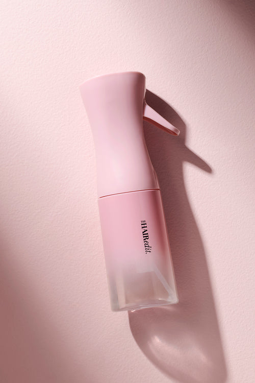 Pink spray bottle with 'The Hair Edit' branding on the bottle on a light pink background